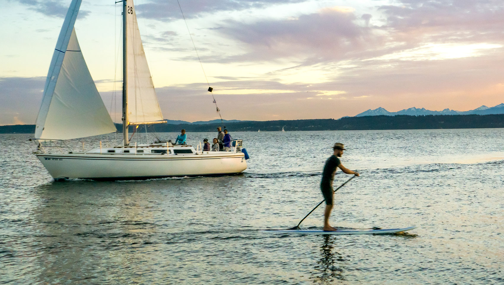 man paddle boarding on the water with a sailboat in the background